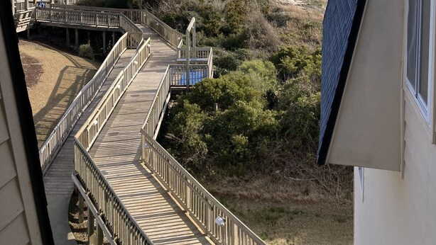 Une vue depuis un balcon donnant sur une plage, une terrasse en bois et un bâtiment doté d’un toit en pente.