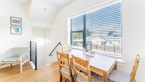 A dining area with a wooden table and chairs, a window with blinds, and a view of the outside.