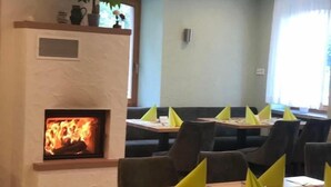 A restaurant with a fireplace, tables with yellow napkins, and a green wall. - Hotel Bischoff (Winnweiler)