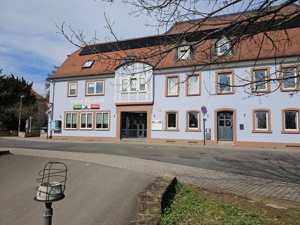 Un immeuble de deux étages avec une enseigne indiquant « Hôtel Bischoff » et « Pizzeria ».