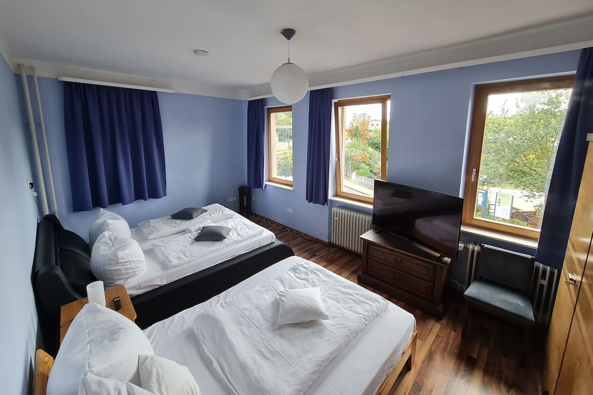 A bedroom with two beds, a TV, a wooden dresser, and a window with a view of trees.