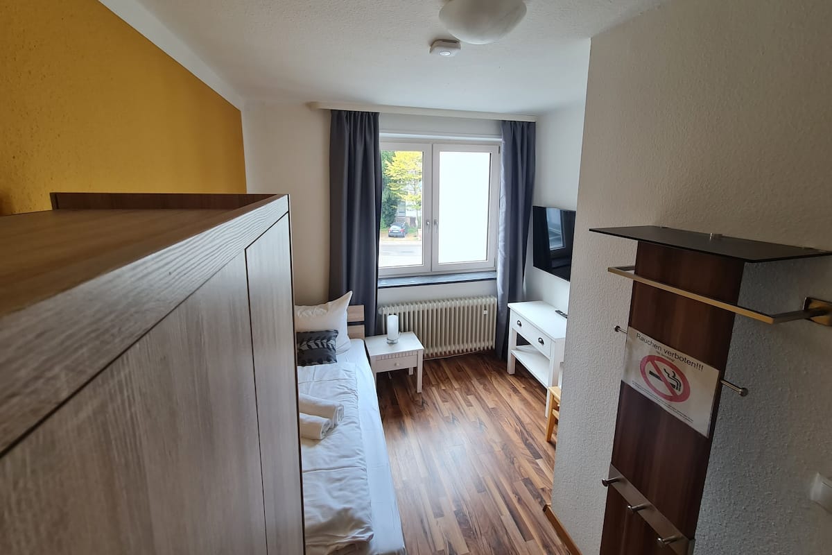A compact hotel room with a bed, bedside table, TV, and a view of the street.