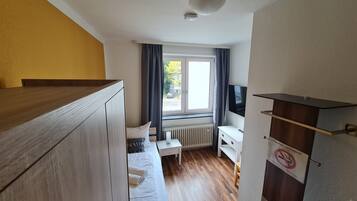 Ein kleines Hotelzimmer mit Bett, Nachttisch, Fernseher und Blick auf die Straße.