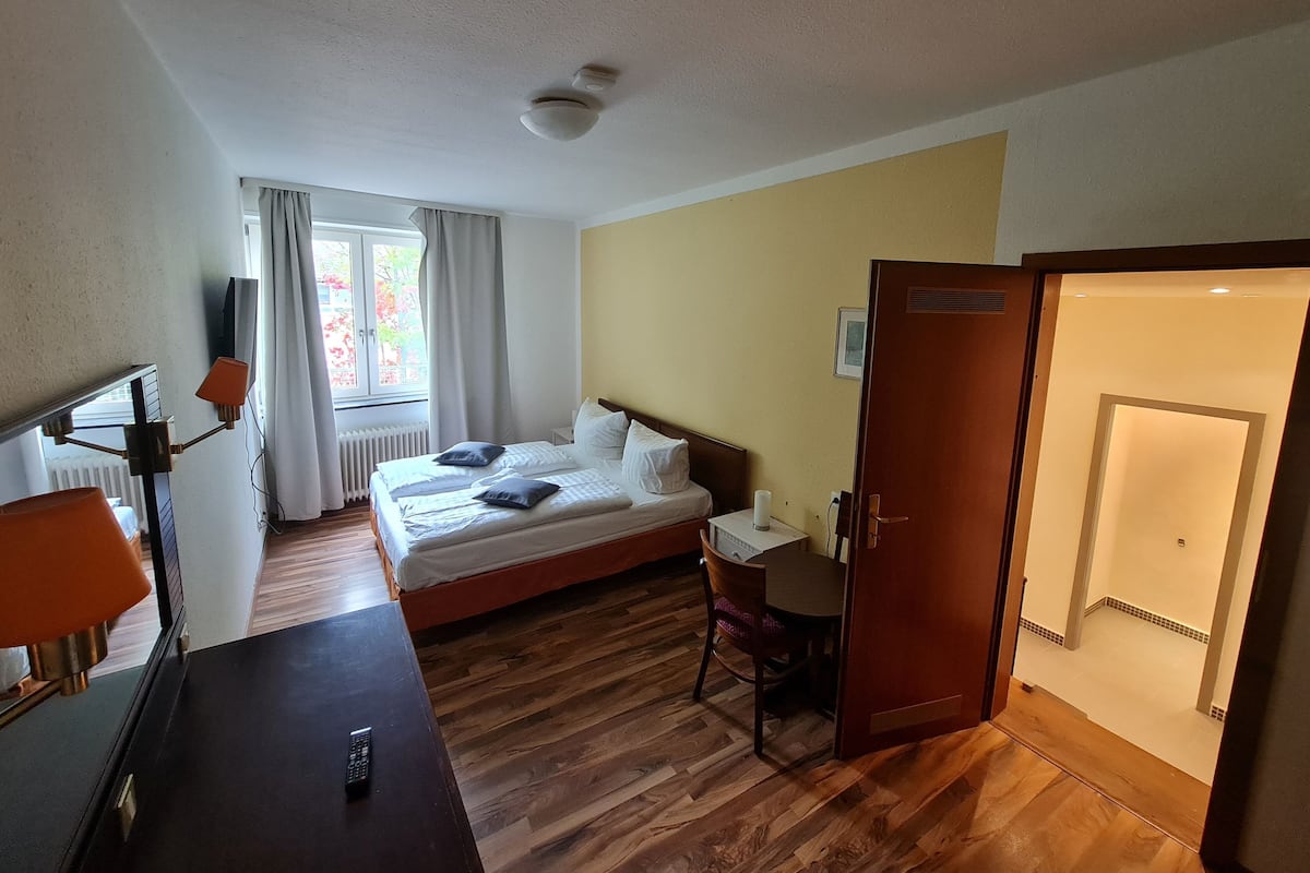 A hotel room with a bed, bedside table, lamp, chair, and a desk with a chair.