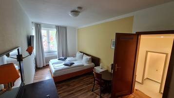 Quarto de hotel com cama, mesa de cabeceira, luminária, cadeira e escrivaninha com cadeira.