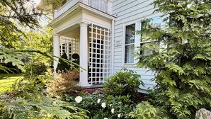 Una casa de dos pisos amb un porxo cobert, envoltada de vegetació exuberanta i un jardí ben cuidat.