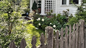 A white house with a porch, a wooden fence, and a garden with white flowers. - Step into History, Stay Close to Downtown!  (Providence)