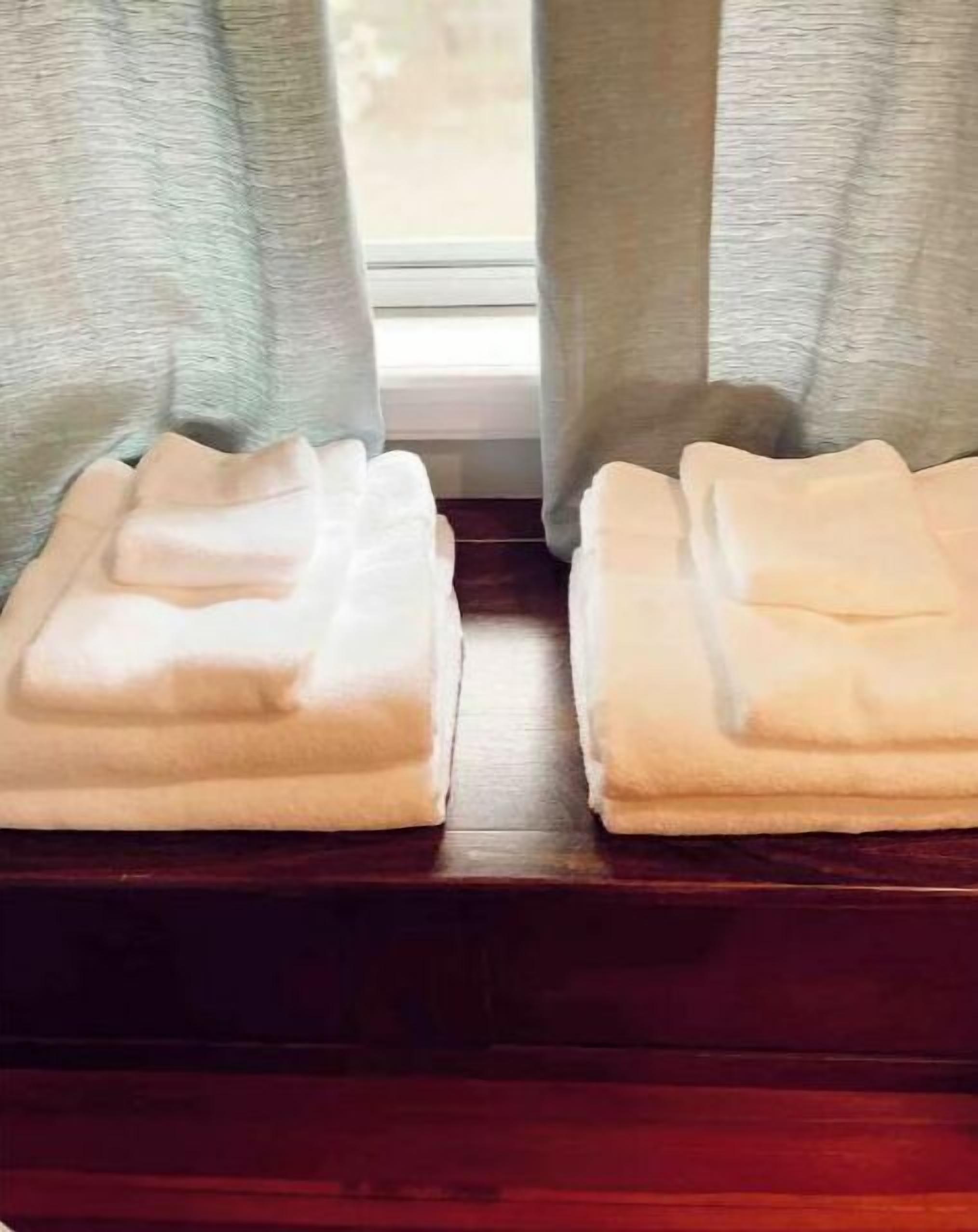 A window with light-colored curtains and two folded white towels on a wooden ledge.