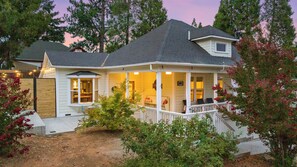 A two-story house with a porch, a covered front porch area, and a small attached garage. - Historic Gold Rush Cottage - Amazing Porch, Patio & Walk to Downtown (Grass Valley)