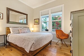 Une chambre avec un lit en bois, un grand miroir, une fenêtre avec des volets et une chaise.