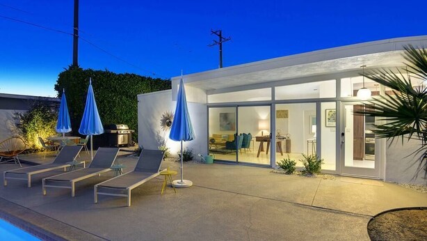 Une maison moderne avec une piscine, des chaises longues et des parasols.