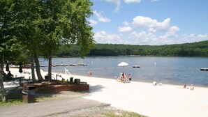 Une plage au bord d’un lac, avec des tables de pique-nique, un quai pour bateaux et des gens qui se détendent.