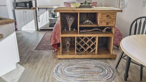 Une cuisine de taille réduite avec des meubles blancs, un four à micro-ondes et une table en bois recouverte d’une nappe à motifs rouges et blancs.