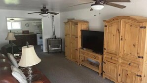 Una sala de estar con un sofá de cuero marrón, un televisor sobre un mueble de madera, un ventilador de techo y una chimenea.