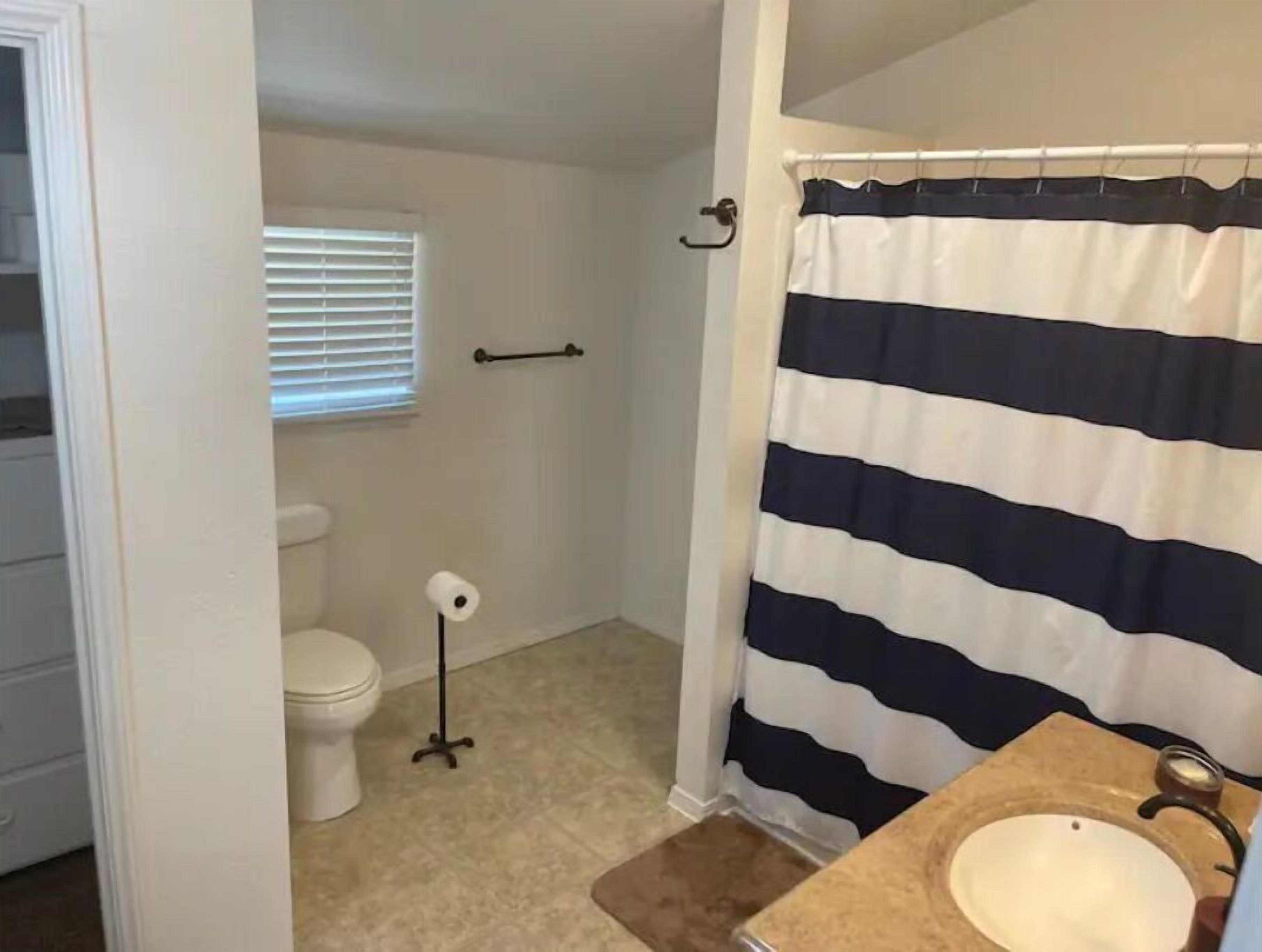A bathroom with a striped shower curtain, a toilet, a sink, and a window with blinds.