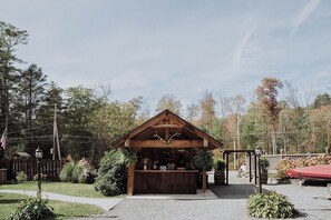 Relax in a serene outdoor setting, surrounded by trees and shrubs, near a rustic bar or reception area with a wooden counter.