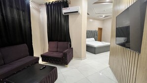 Ein modernes Hotelzimmer mit einer Couch, einem kleinen Tisch, einem Bett und einem an der Wand montierten Fernseher.