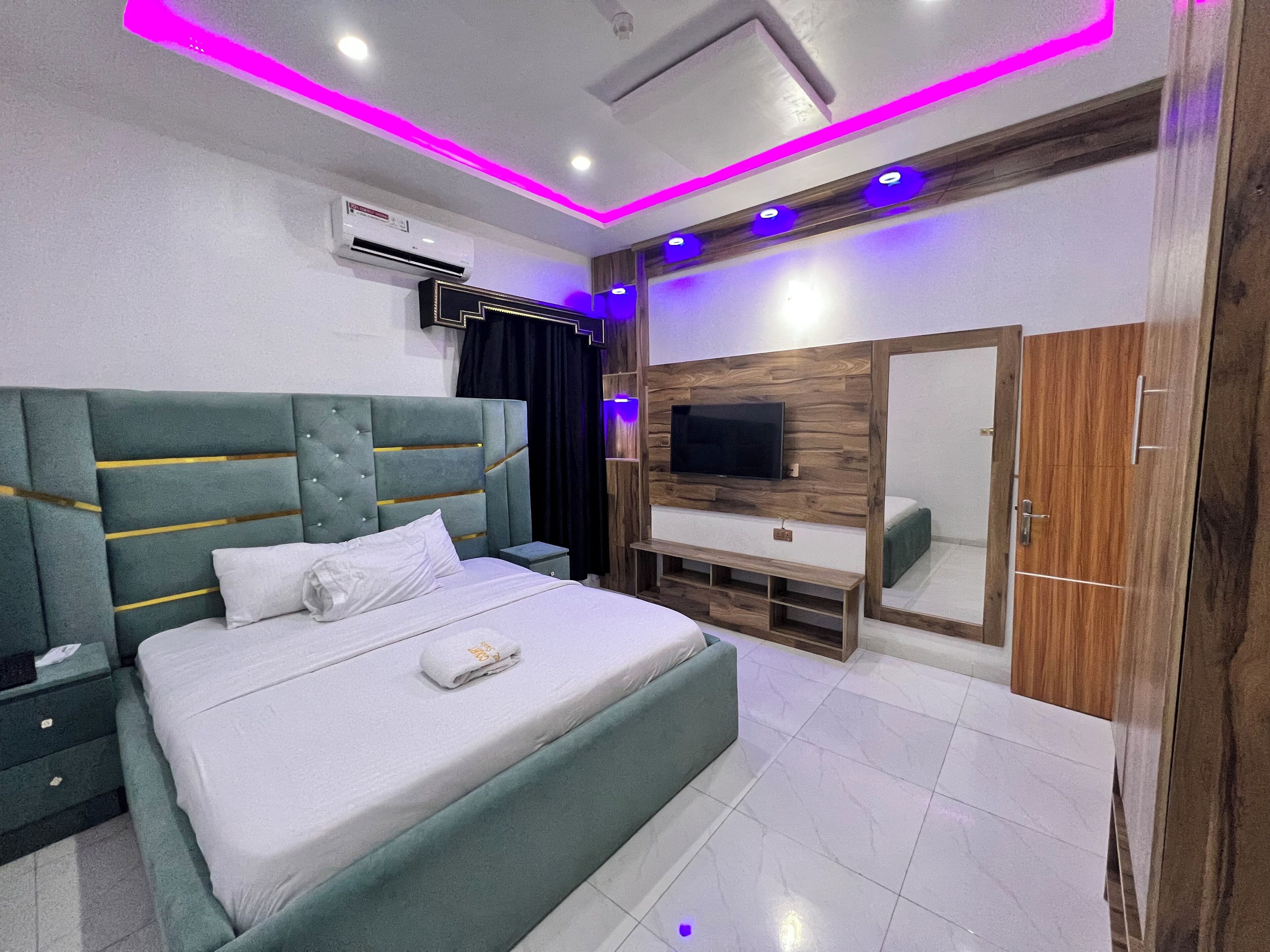 Un dormitorio moderno con cama, televisor, armario y aire acondicionado.