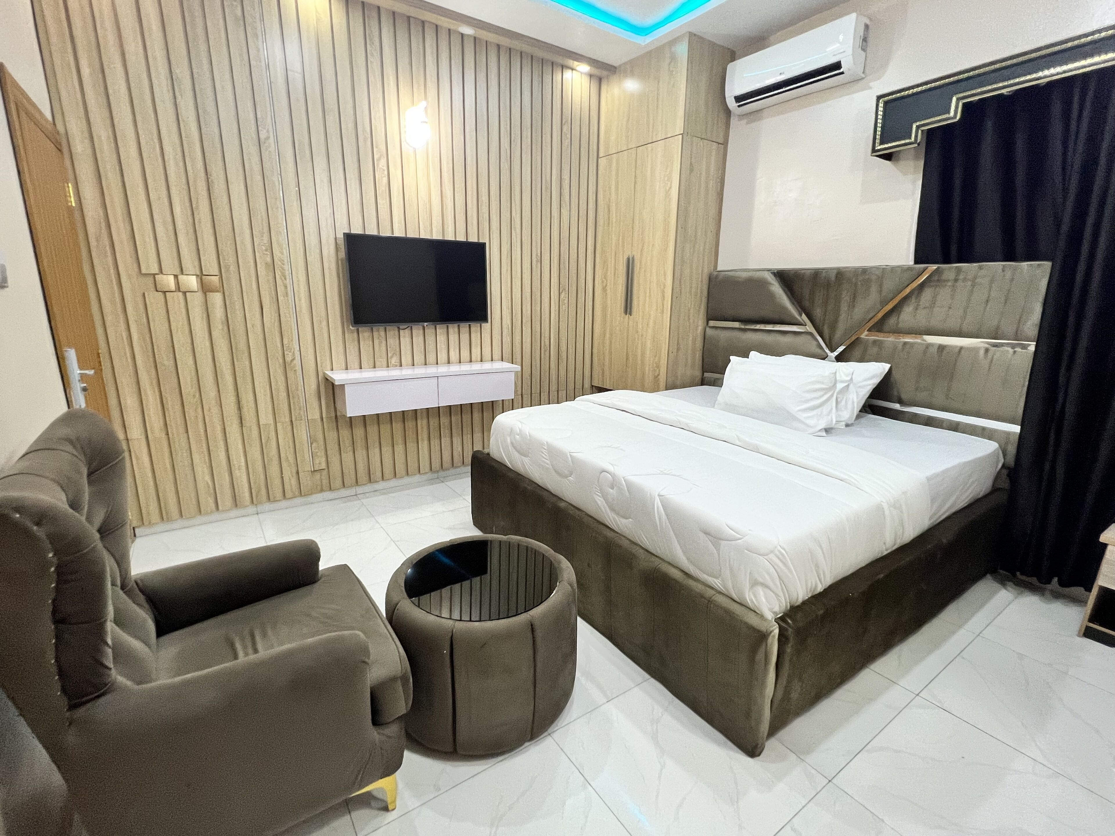 A modern bedroom with a bed, a sofa, a TV, and a wall-mounted shelf.