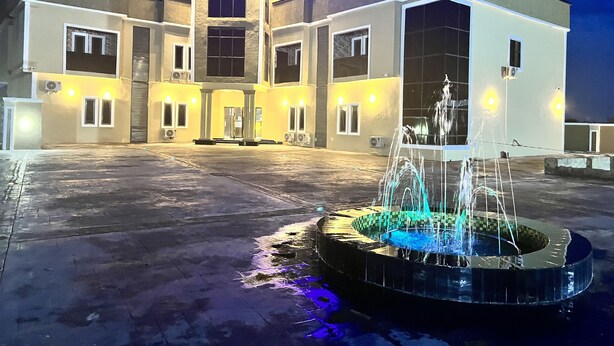 Ein modernes Gebäude mit einem zentralen Eingang, einem Brunnen und einem großen Parkplatz.