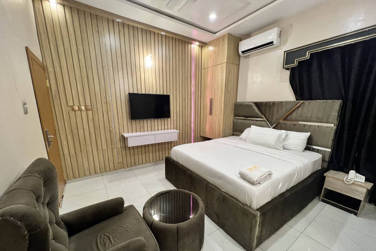 Ein modernes Hotelzimmer mit einem großen Bett, einem flachbildfernseher an der Wand, einem Nachttisch mit Telefon und einer Sitzecke mit Sofa und rundem Tisch.