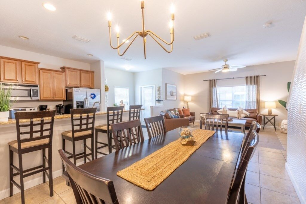 A modern kitchen with wooden cabinets, a dining area with a dark wooden table, and a chandelier.