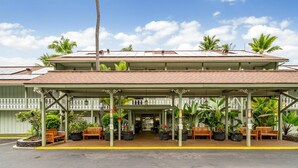 A hotel with a covered entrance, outdoor seating, and tropical plants.