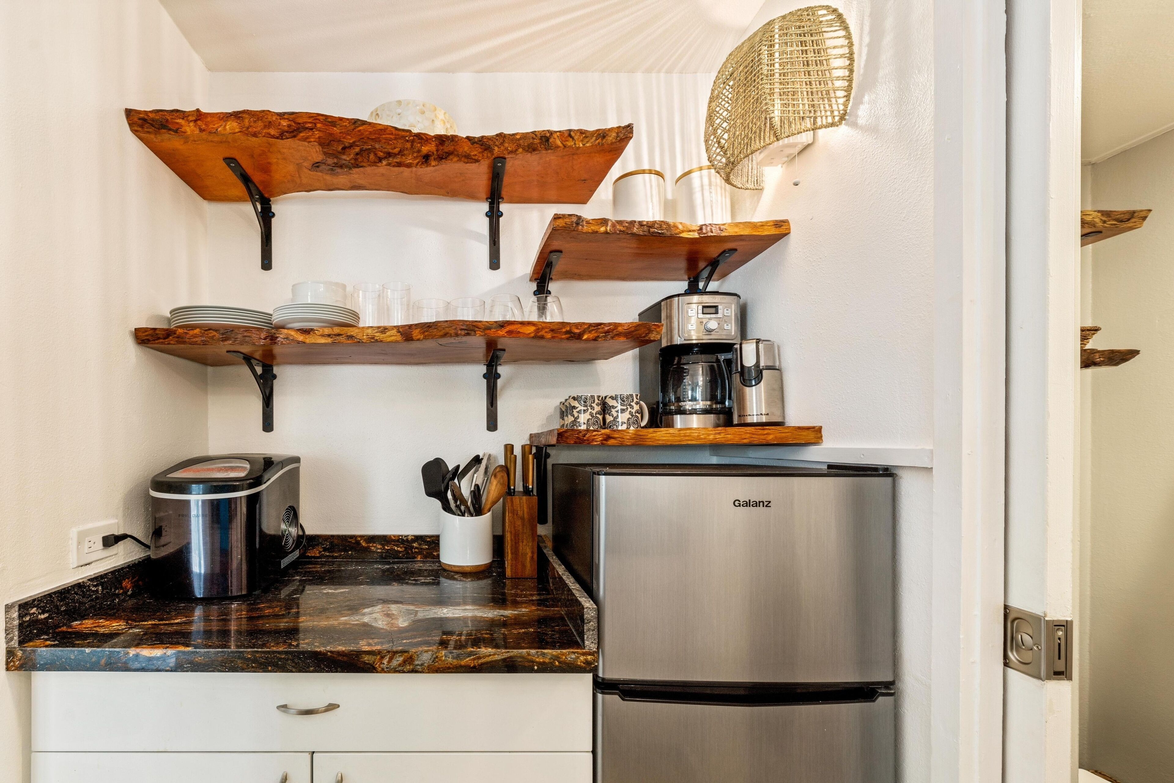 Uma cozinha com geladeira Galanz, prateleiras de madeira, cafeteira e pia.
