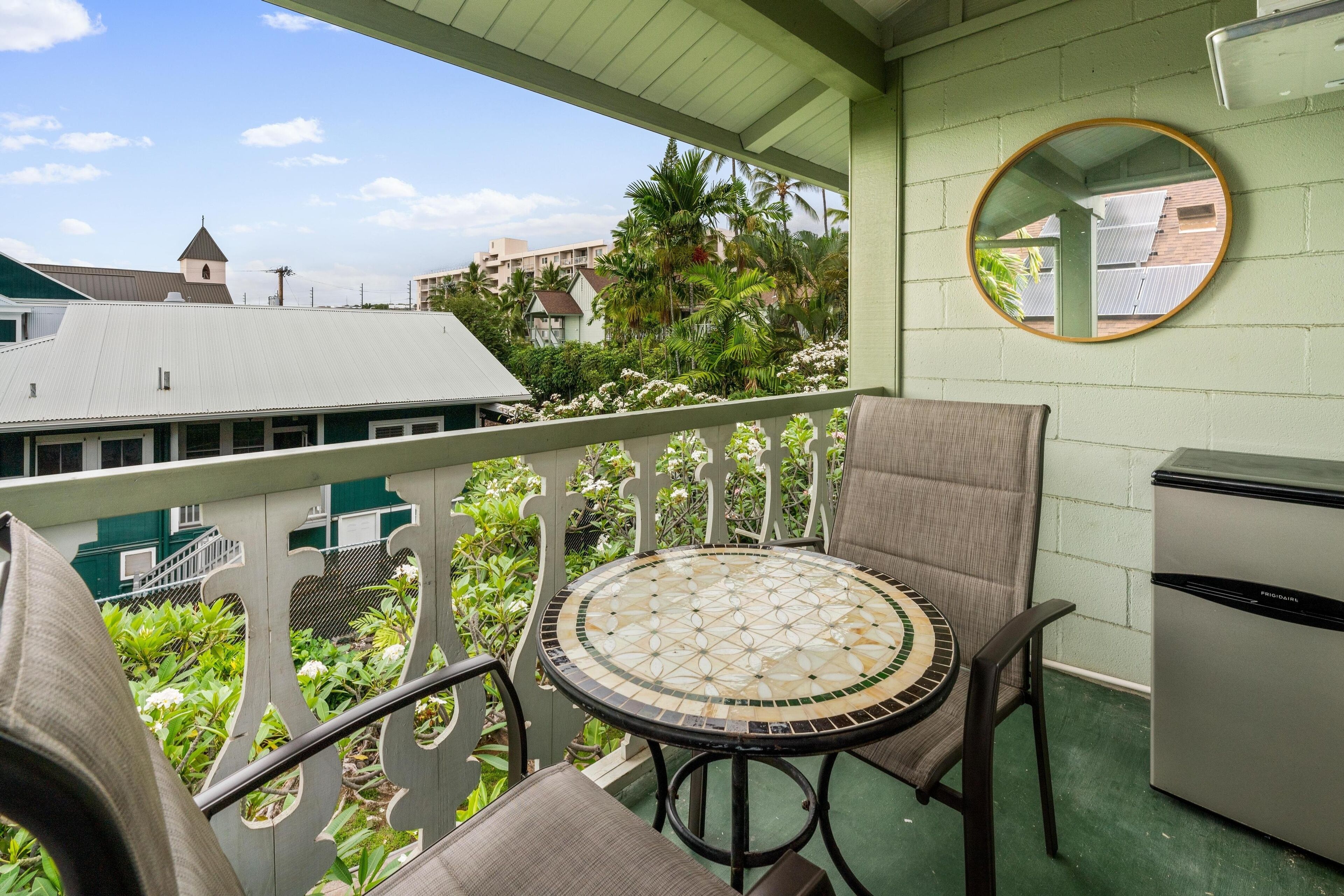 A balcony with a round table and chairs, a small refrigerator, and a mirror on the wall.