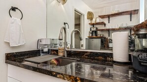 A kitchen with a black marble countertop, stainless steel sink, and a coffee maker.
