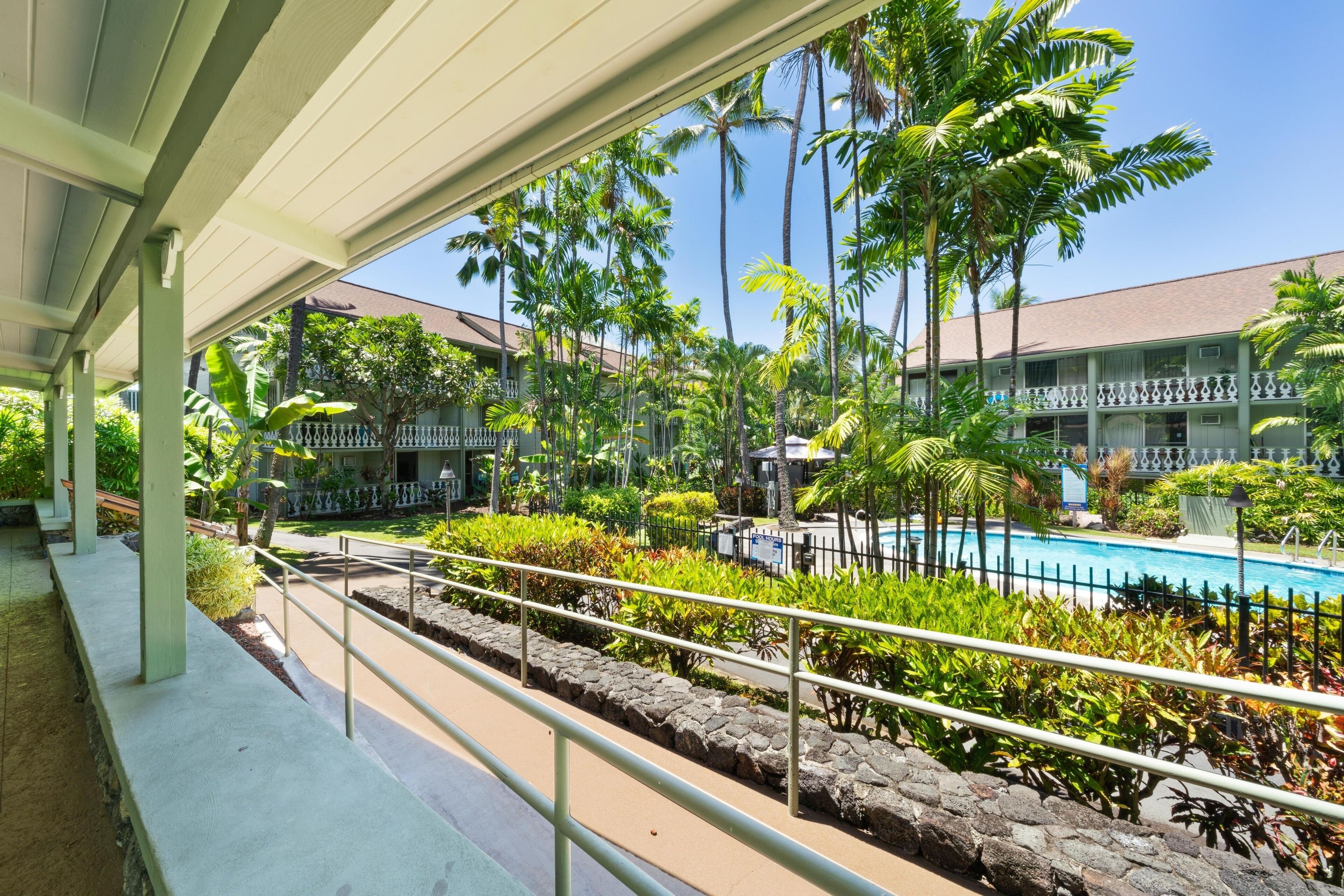 A hotel with a pool, palm trees, and a covered walkway.