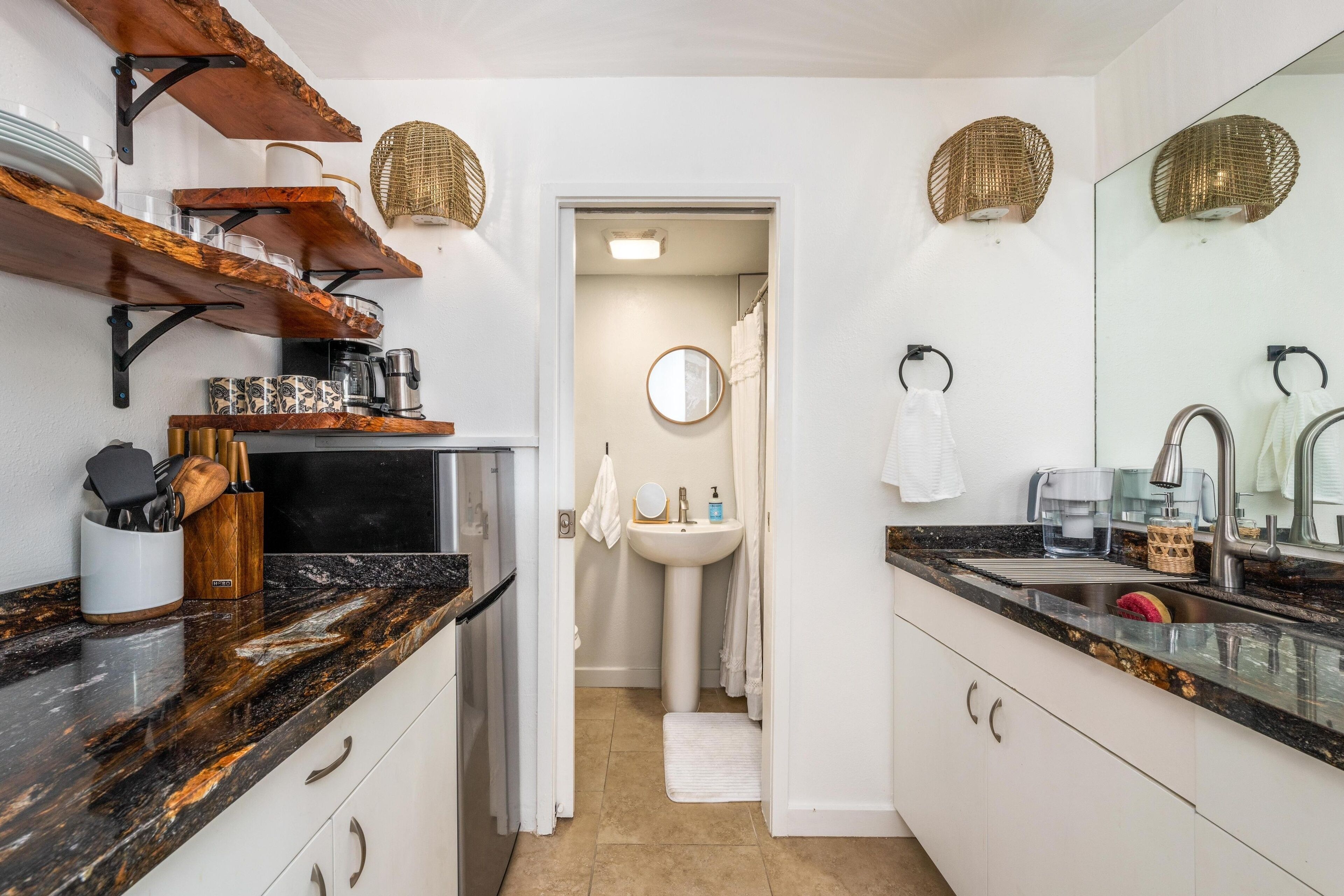 A modern kitchen with dark granite countertops, wooden shelves, and a coffee machine.