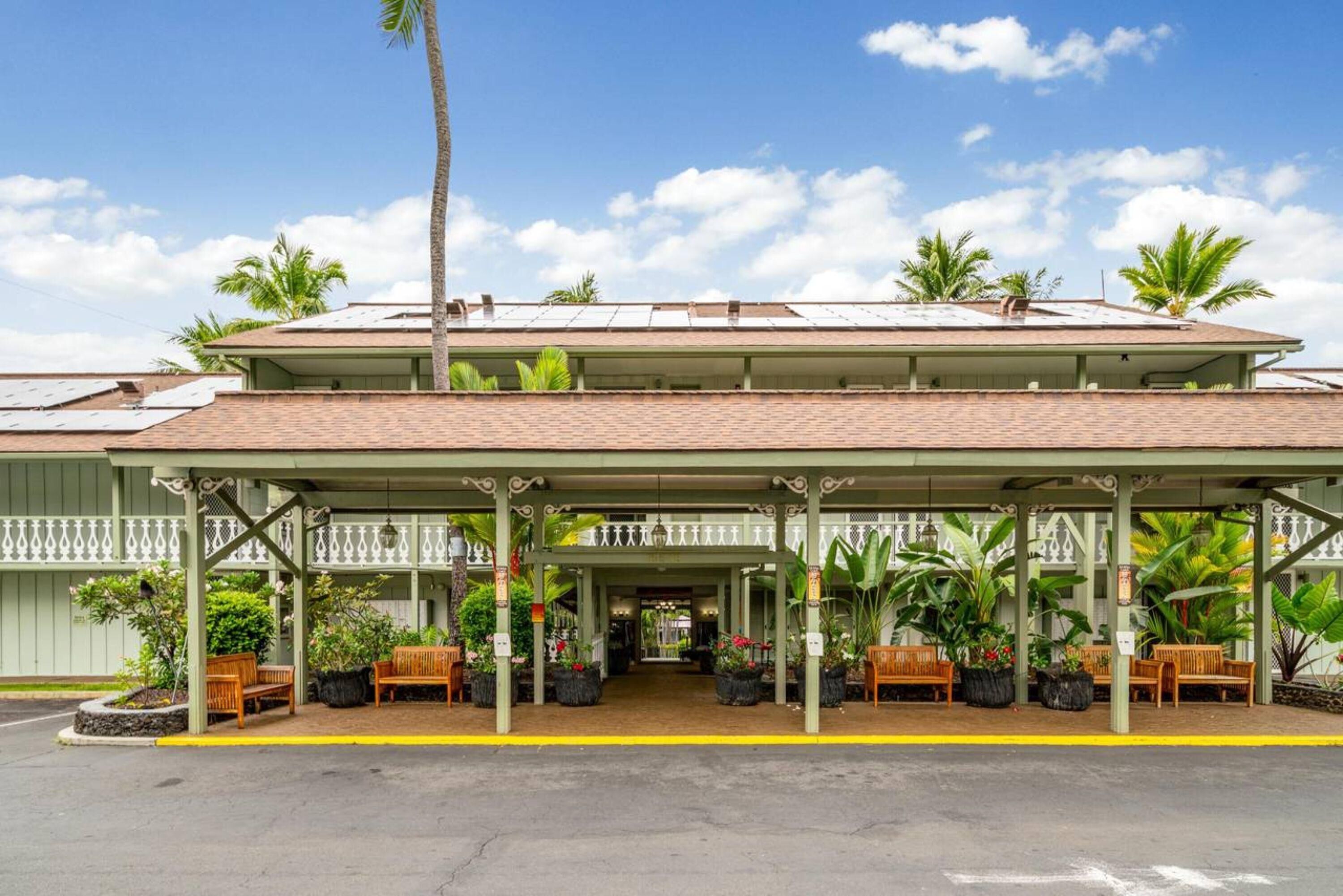 Un hotel con entrada cubierta, mesas al aire libre y palmeras.