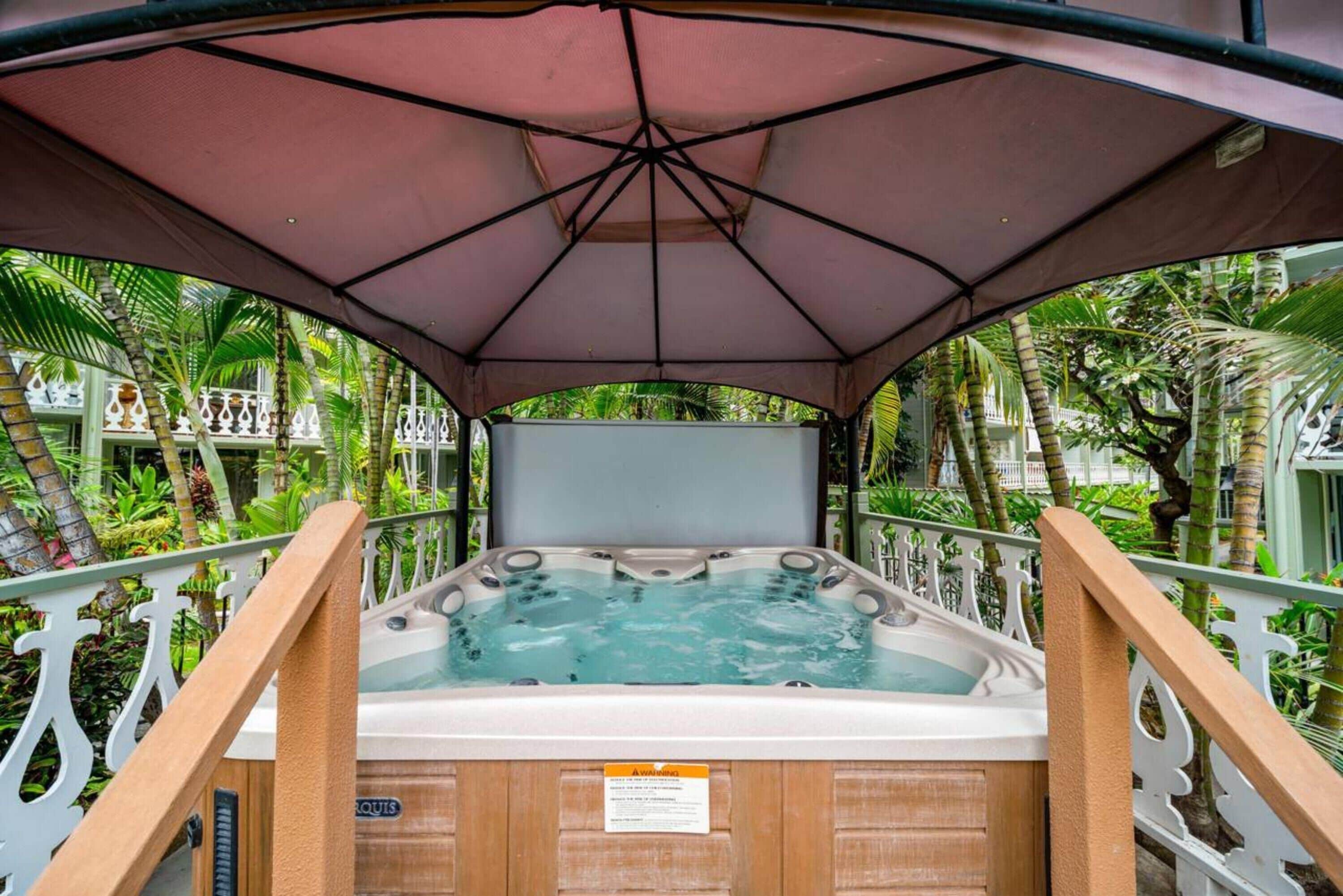 Un bain à remous installé sous une pergola avec une rambarde en bois, entouré d’une végétation luxuriante.