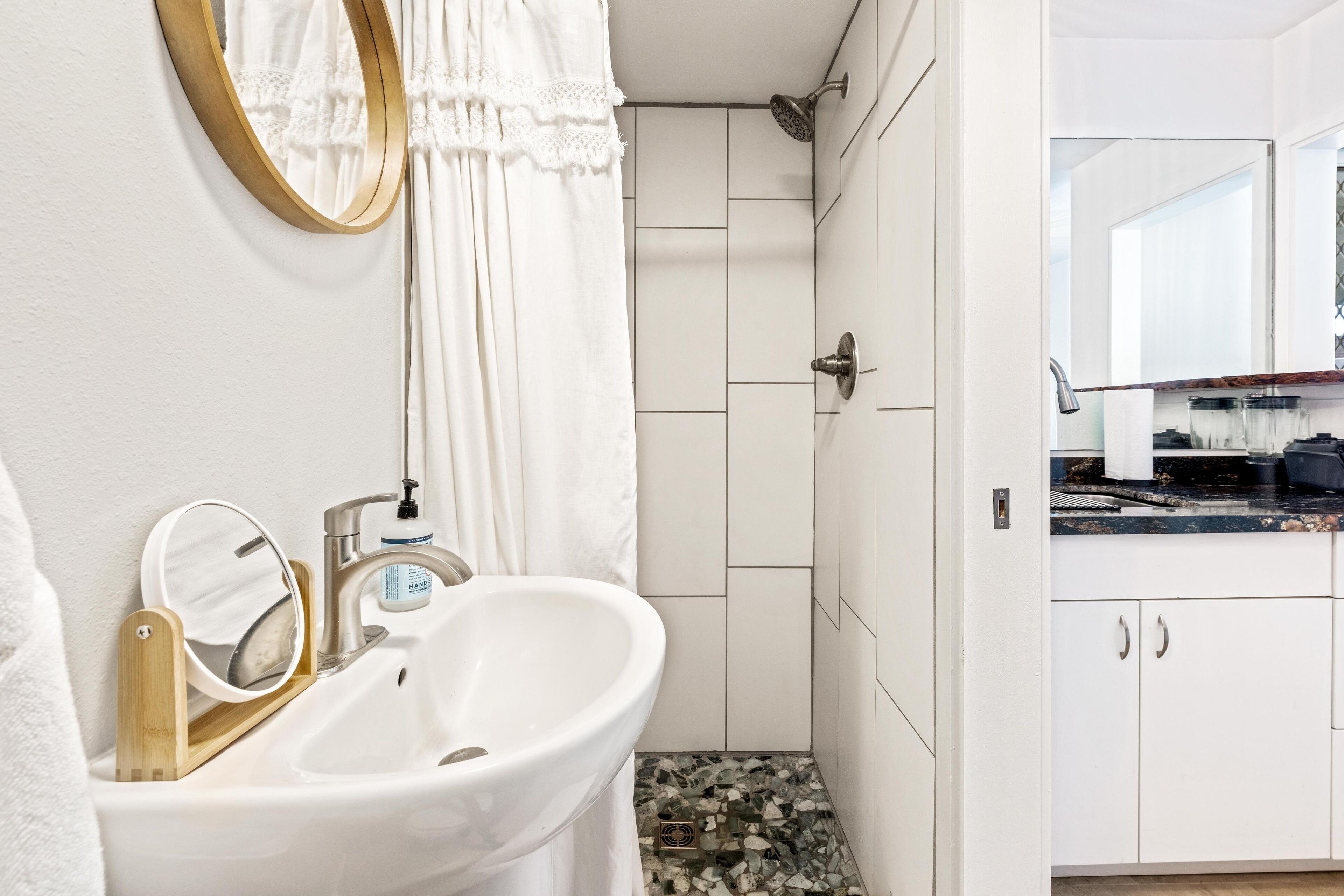 A bathroom with a white sink, a mirror, a shower, and a tiled floor.