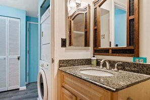 Un baño con lavamanos de encimera de granito, espejo con marco de madera y lavadora.