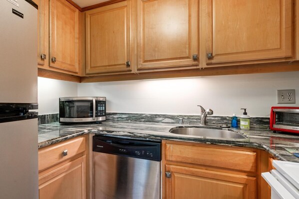 Una cocina con armarios de madera, lavavajillas de acero inoxidable, microondas, un lavabo y un tostador rojo.