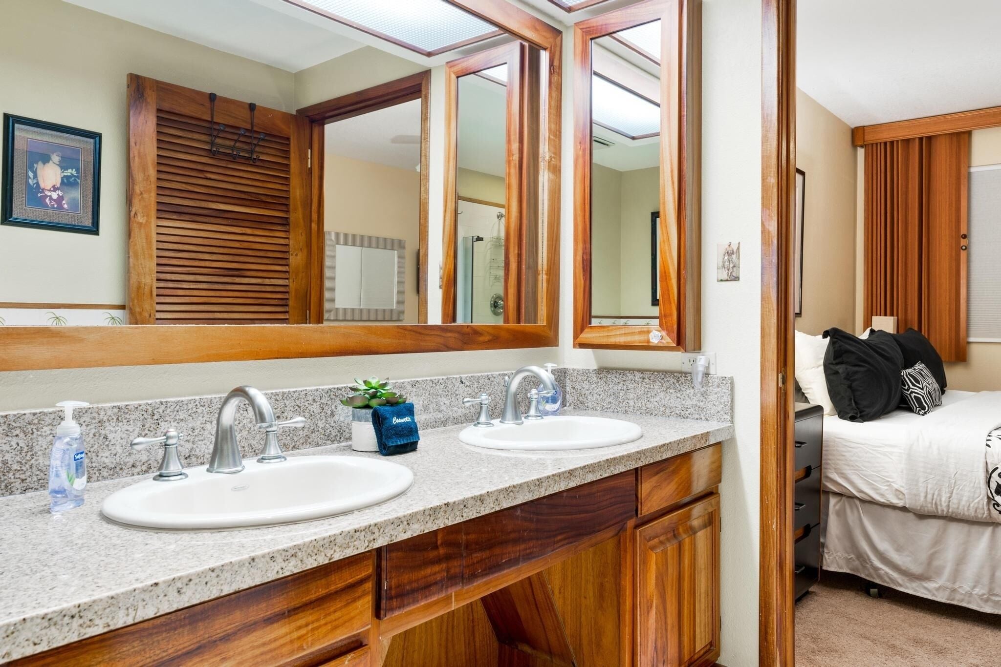 A bathroom with two sinks, wooden cabinets, a large mirror, and a bed with pillows.