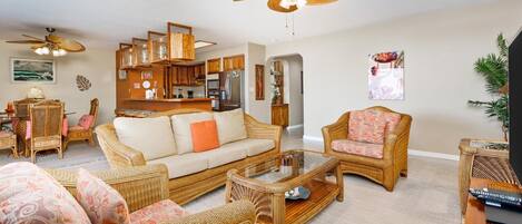 A spacious living room with wicker furniture, a glass coffee table, and a ceiling fan.