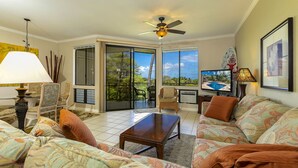 A spacious living room with a large window, a ceiling fan, and a television.