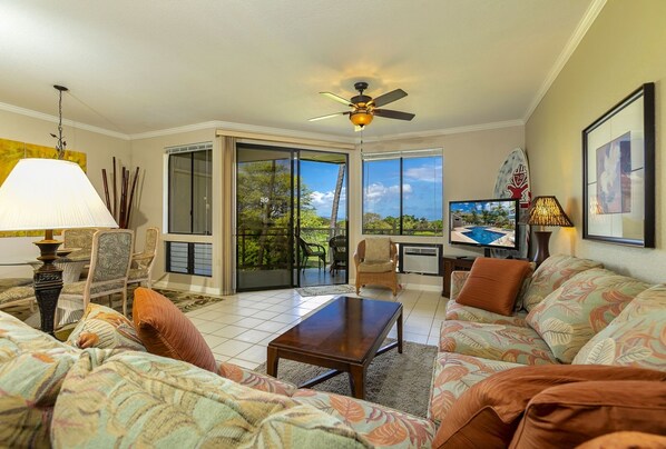A spacious living room with a large window, a ceiling fan, and a television. - Grand Champions One Bedrooms by Coldwell Banker Island Vacations (Kihei)