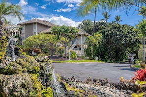 A residential area with a house featuring a balcony, a small waterfall, and lush greenery.