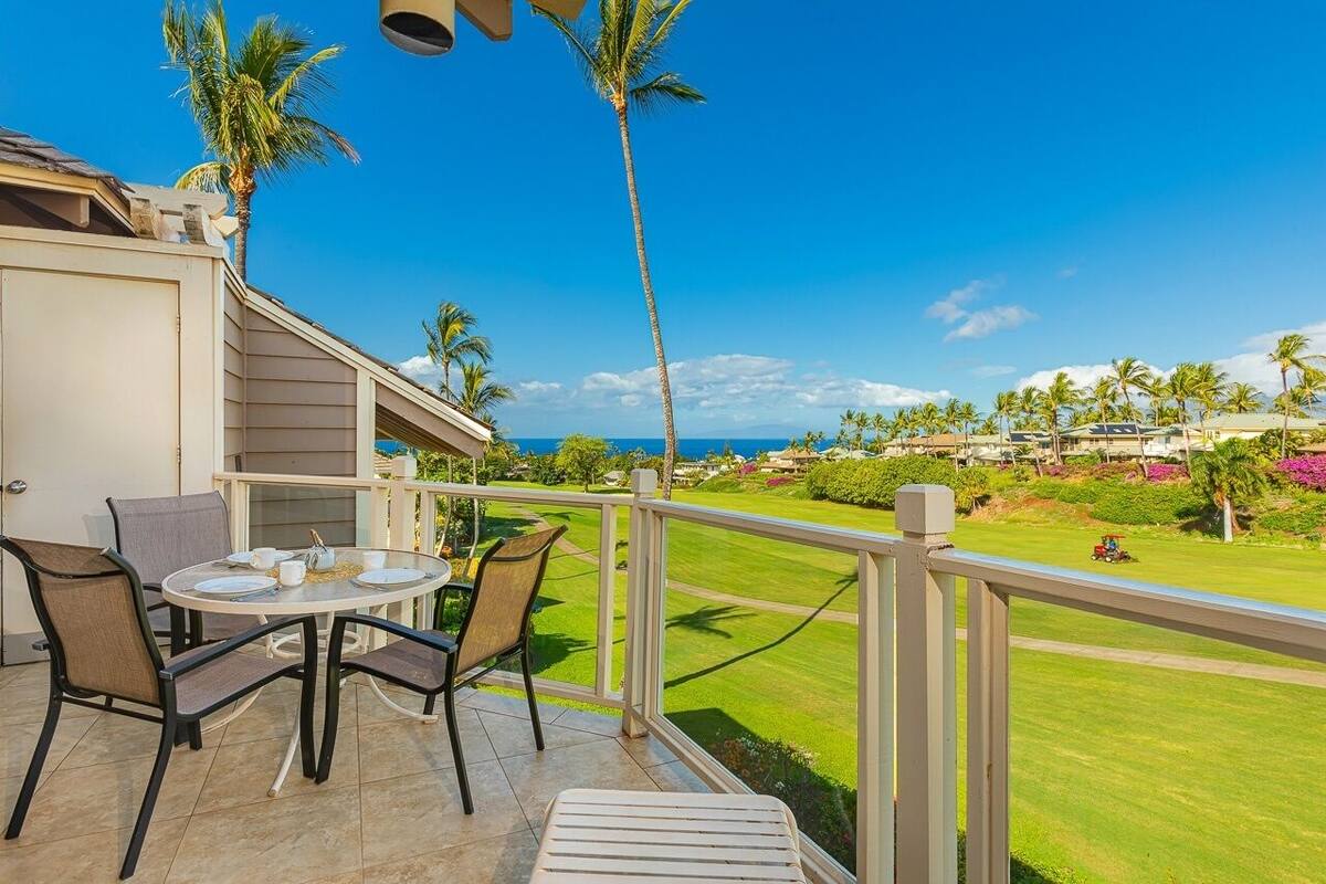 Ein Balkon mit Tisch und Stühlen, der auf eine gepflegte Rasenfläche und den Blick aufs Meer bietet.