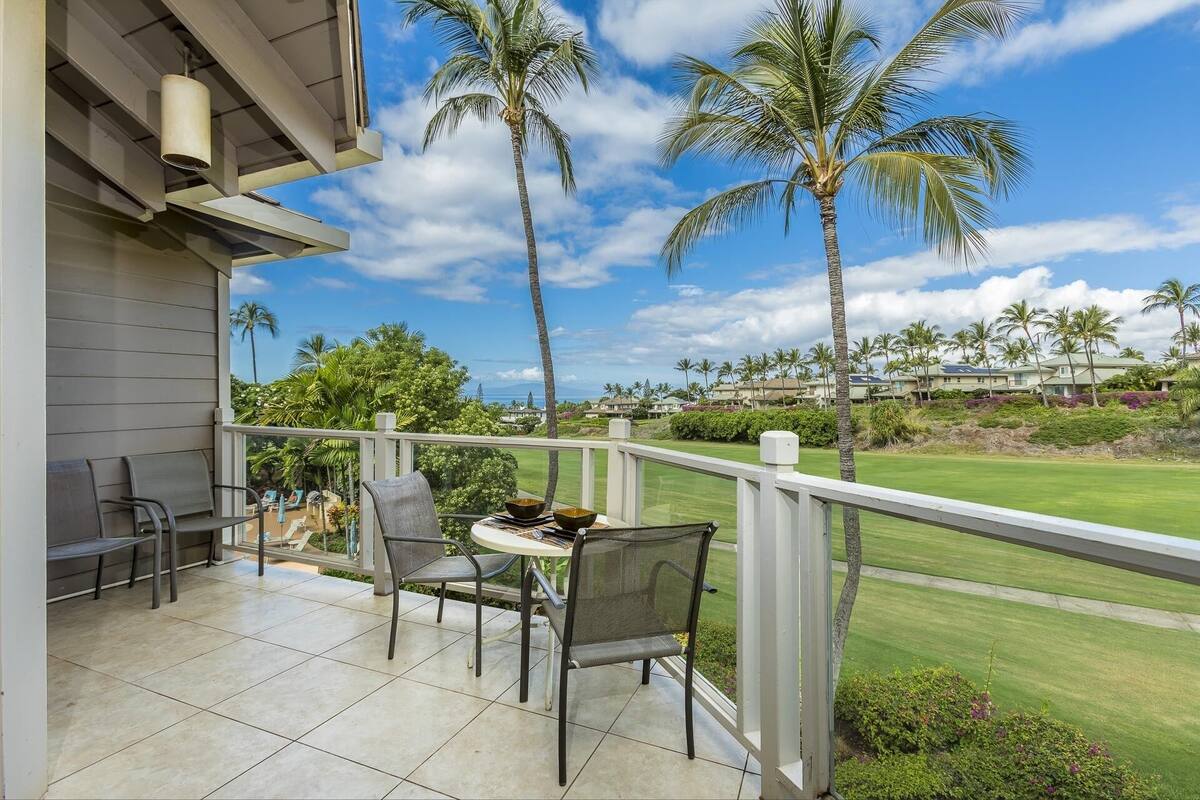 Ein Balkon mit Tisch und Stühlen, mit Blick auf einen Golfplatz und Palmen.