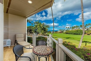 A balcony with two chairs and a table, overlooking a golf course and palm trees.