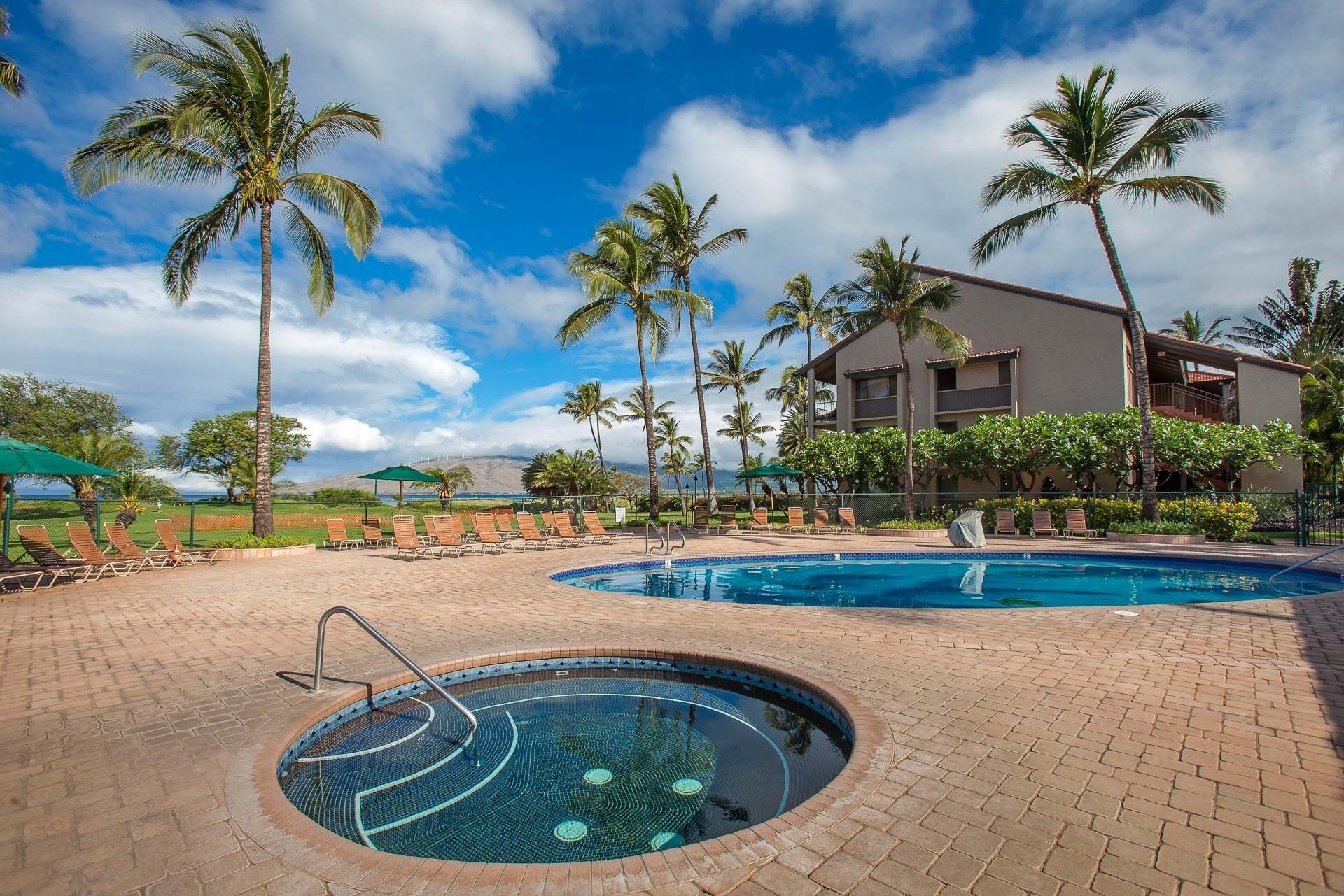 A pool area with lounge chairs and palm trees, surrounded by a building with balconies.