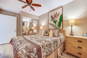 A bedroom with a bed, bedside tables, a ceiling fan, and a large mirror. - Kihei Surfside, #107 1 Bedroom Condo by RedAwning (Kihei)