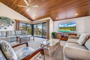 A spacious living area with a ceiling fan, a large window with a view of palm trees, and a flat-screen TV. - Wailea Elua, #1404 2 Bedroom Condo by RedAwning (Kihei)