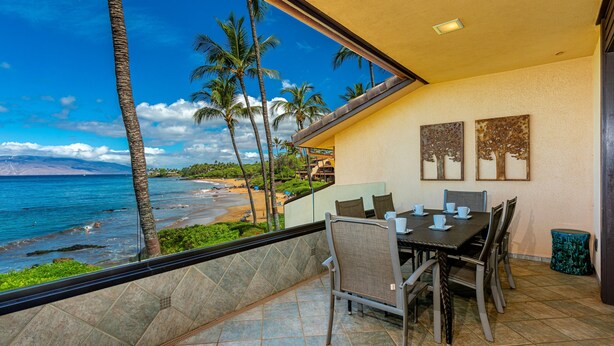 Ein Balkon mit Blick auf Strand und Meer, ein Esstisch mit Stühlen sowie zwei an der Wand befestigte Kunstwerke.