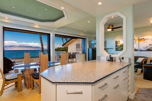 A modern kitchen with a large island, dining area with chairs, and a view of the ocean. - Makena Surf, #e-202 2 Bedroom Condo by RedAwning (Kihei)